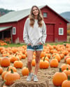 Young Woman in Sweatshirt Standing on Hay Block with Pumpkins Around Mockup